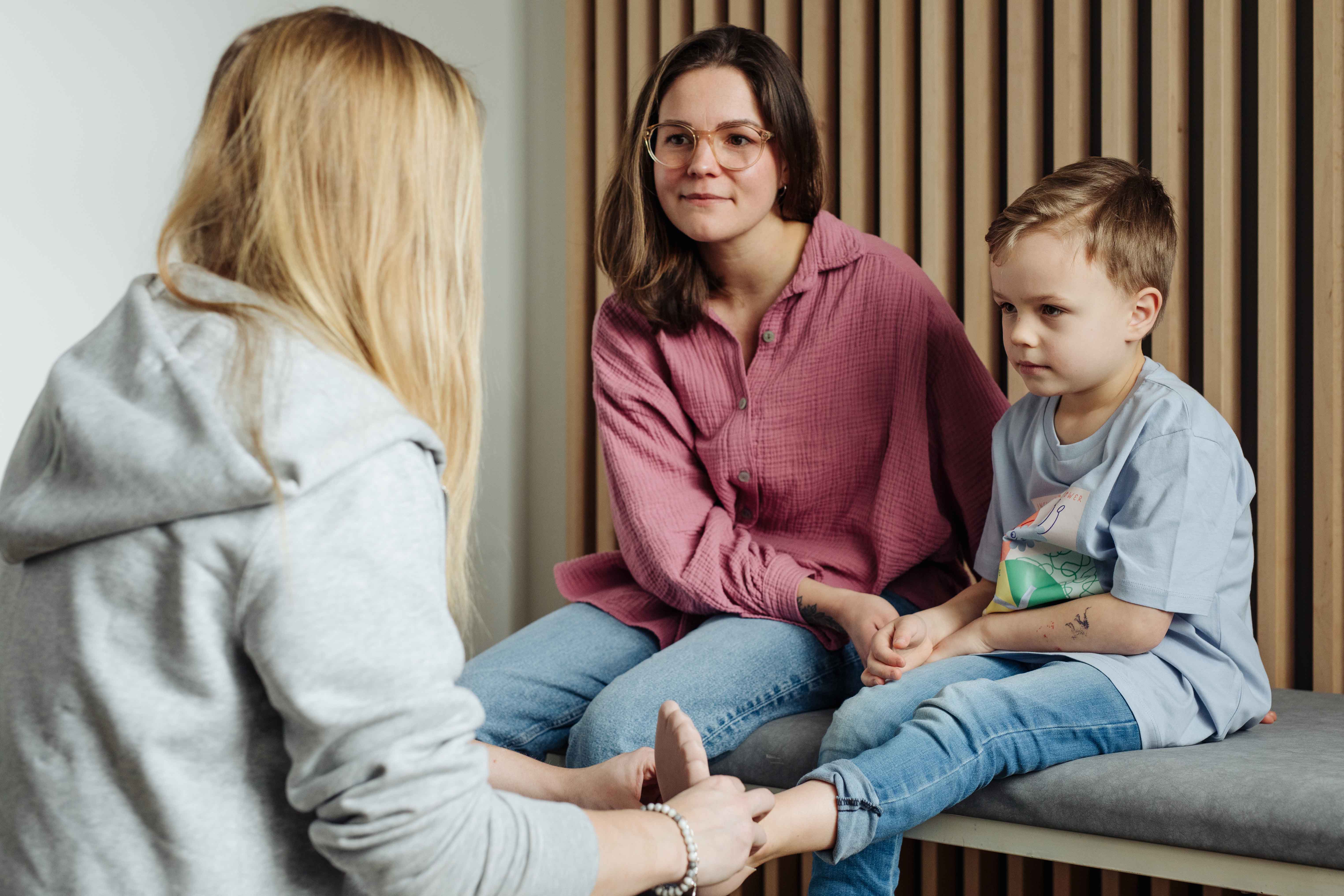 Kathrin von Hodey Kids überprüft den Sitz der Fußprothese eines kleinen jungen, der mit seiner Mutter auf einer Liege Platz genommen hat.
