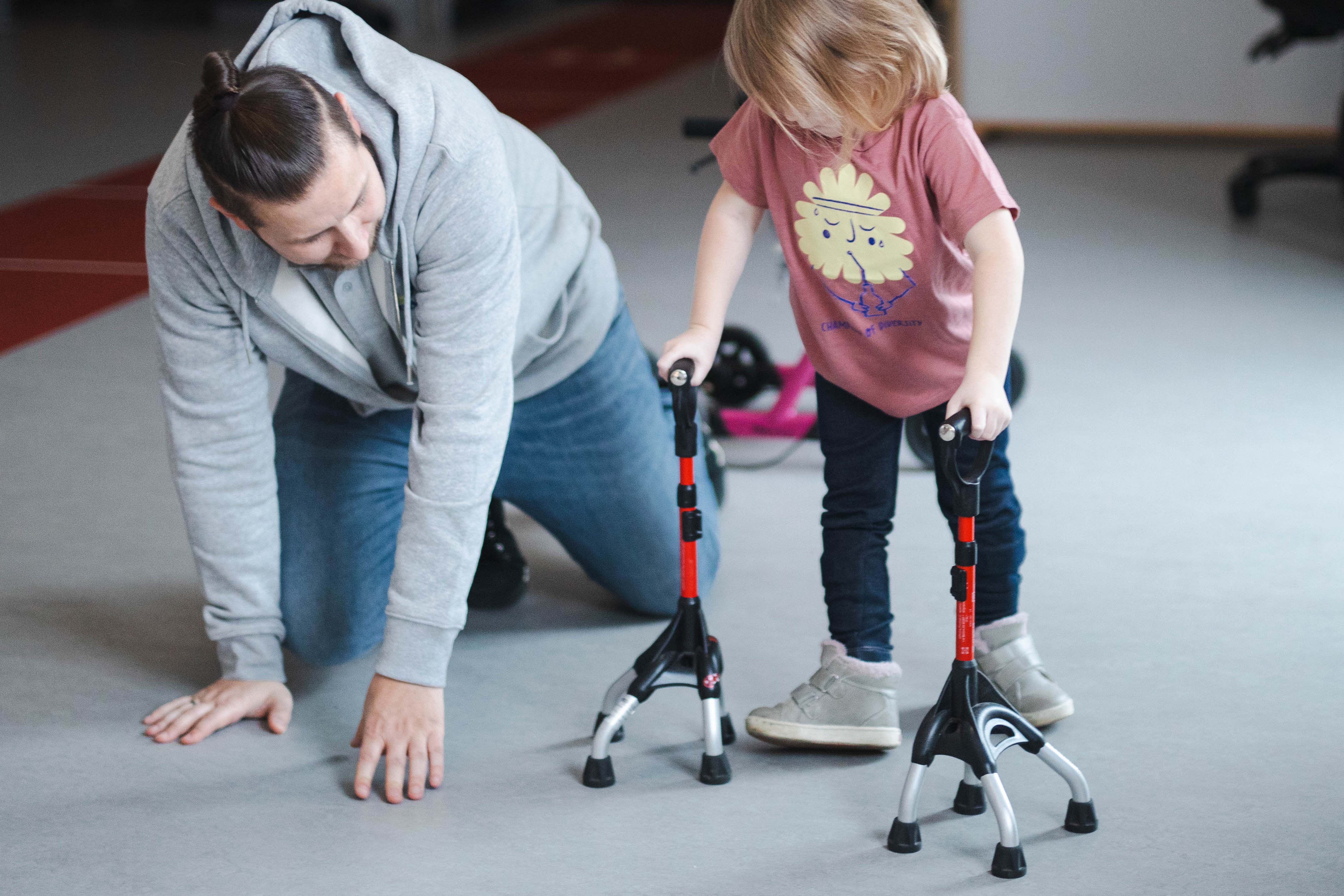 Tobias von Hodey Kids übt mit einem kleinen Mädchen das Fortbewegen mit Gehhilfen.
